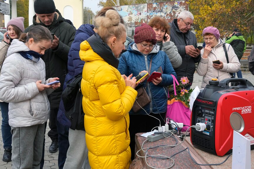 Several people stand around a power generator charging their phones