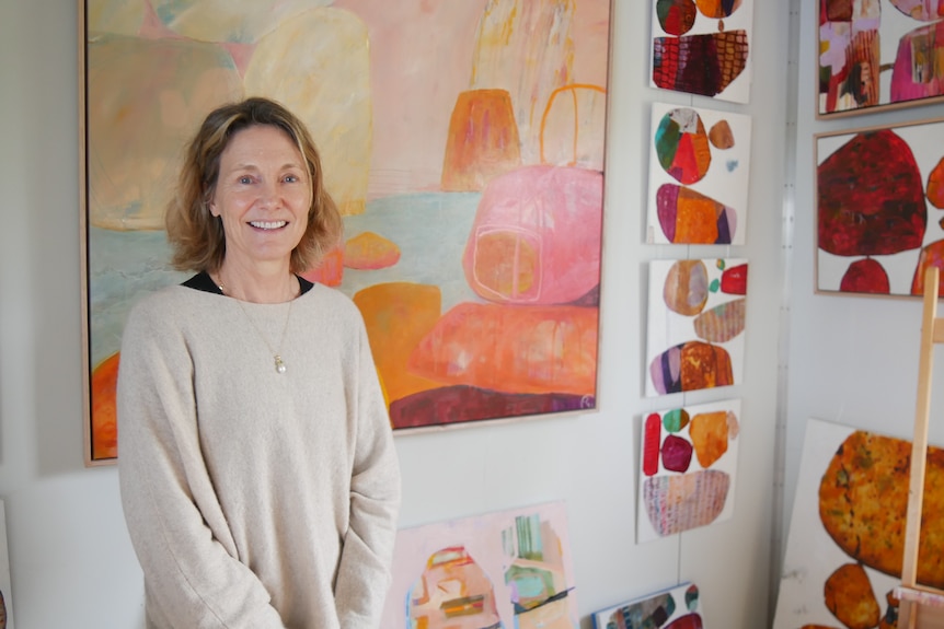 A woman stands in a bright room in front of colourful paintings