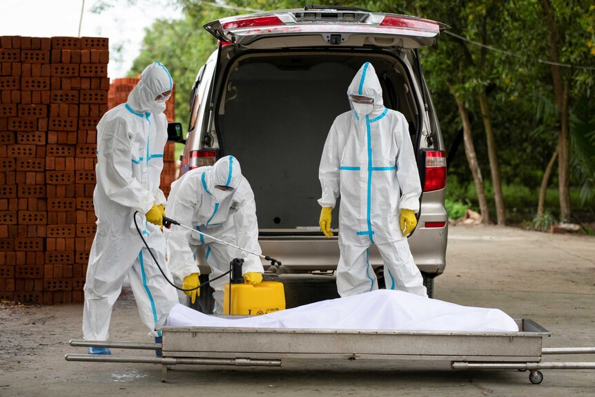 Volunteers wearing personal protective suits disinfect a body of a person who died from COVID-19.