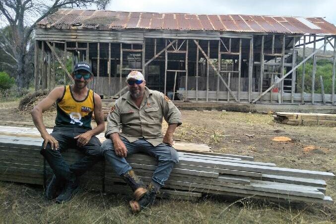Two men sitting on pile of wood.