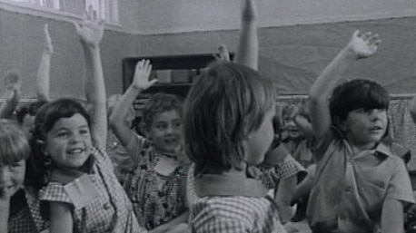 Young children sit in class with raised hands
