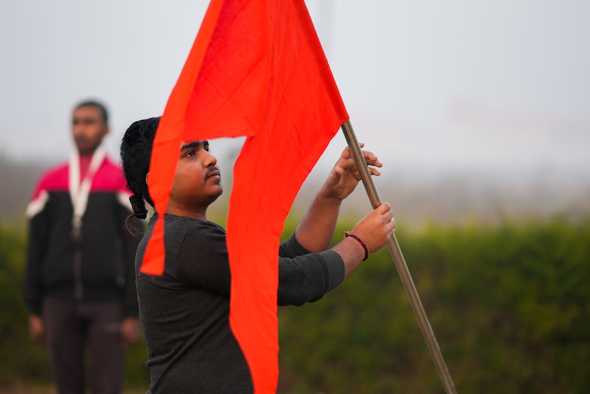 A man handles a pole with an orange flag, it has a split in the middle