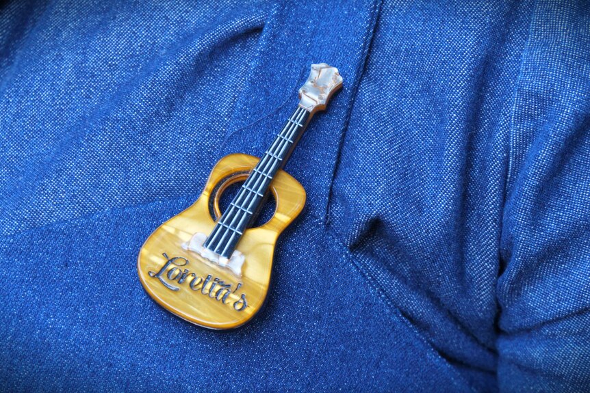 A small guitar broach on a blue denim shirt