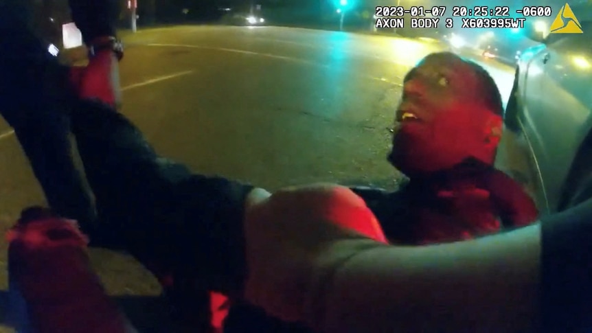 A screenshot shows a young black man looking up at police as he is violently arrested.