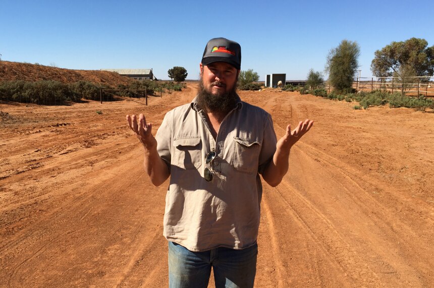 Grazier Nick Andrews shrugging and standing on a red dirt road at Farmcote station.