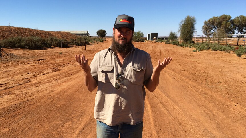 Grazier Nick Andrews shrugging and standing on a red dirt road at Farmcote station.