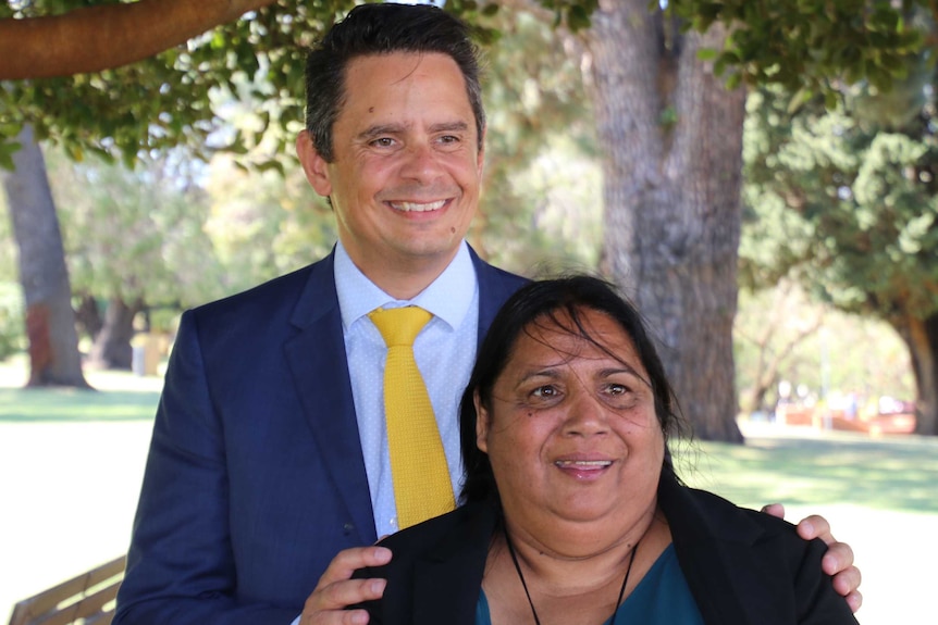 Ben Wyatt standing with his hands on the shoulders of Jeanice Krakouer.  Both smiling for the camera in park setting.