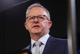 A close shot of Anthony Albanese standing on stage, wearing glasses.