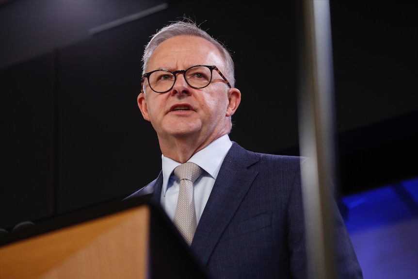 A close shot of Anthony Albanese standing on stage, wearing glasses.