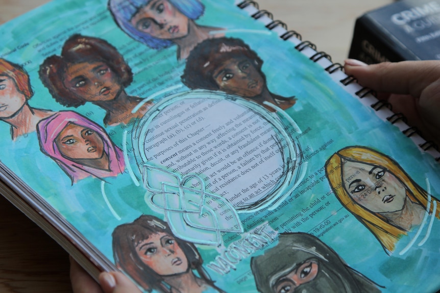 A hand holding a book with blue paint and sketches of women of all colours, some wearing hijab and niqab.