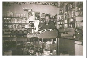 A black and white image showing a man in an old-fashioned shop in front of jars of lollies.