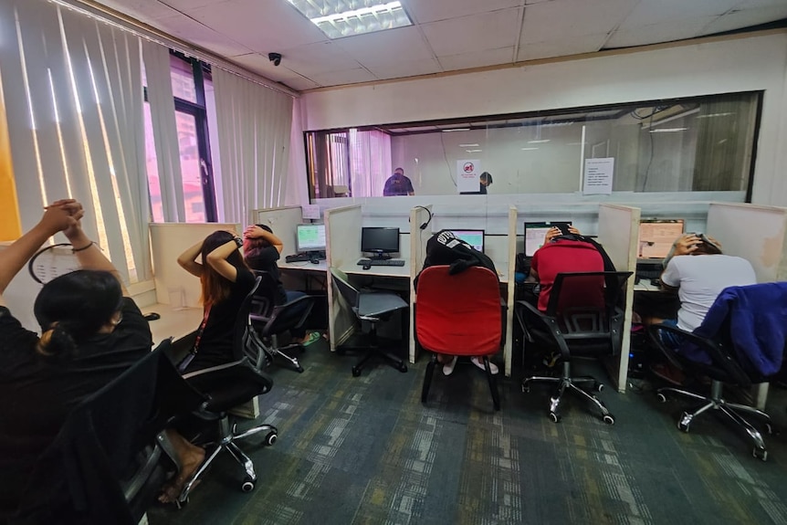 Workers at desks with their hands above their heads.