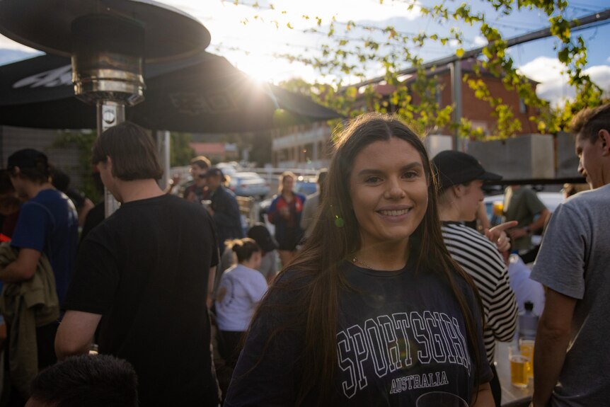 A woman at an outdoor bar smiles at the camera.