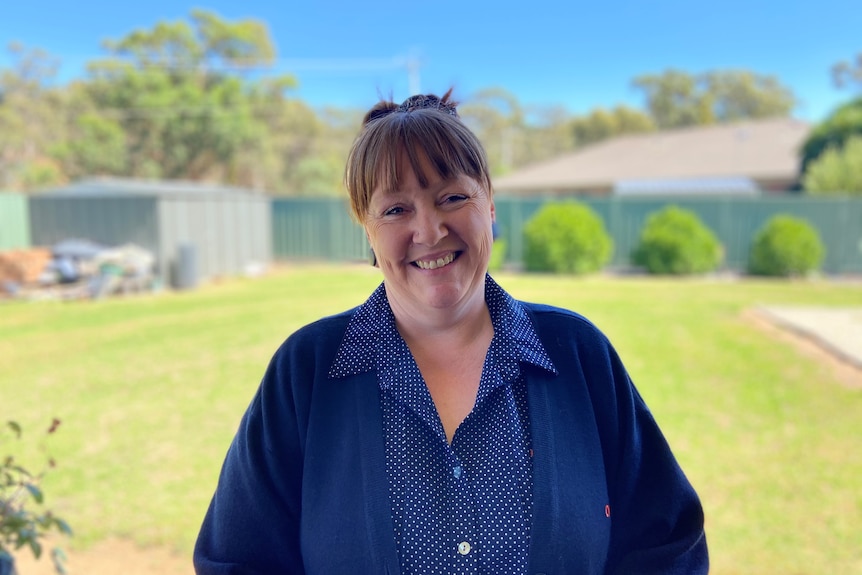 A woman smiling at the camera with backyard in the background. 