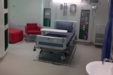 One of the rooms at the hospital with purple bedding and red chairs.