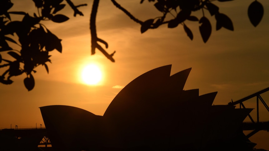 A bright sunset paints the sky orange as the Sydney Opera House is seen below.