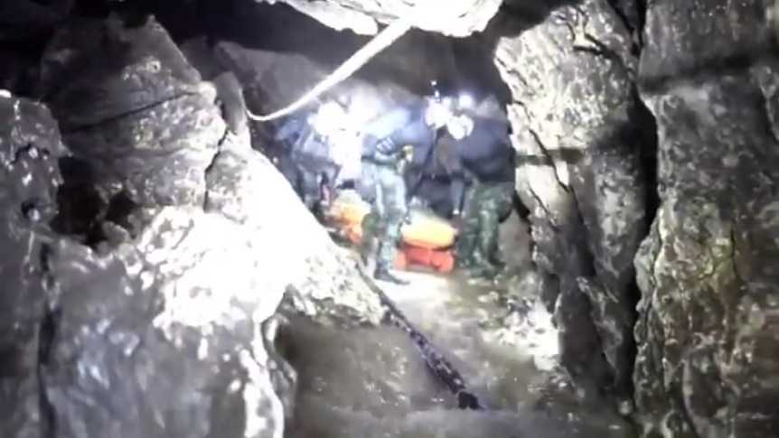 Rescue workers crouch down as they transfer a stretcher through a cave in Thailand.