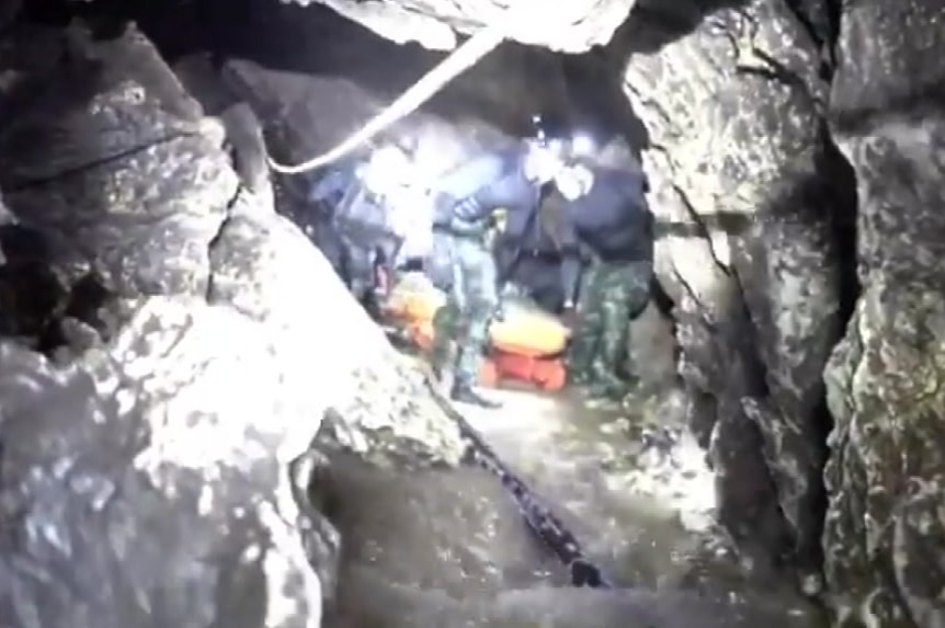 Rescue workers crouch down as they transfer a stretcher through a cave in Thailand.