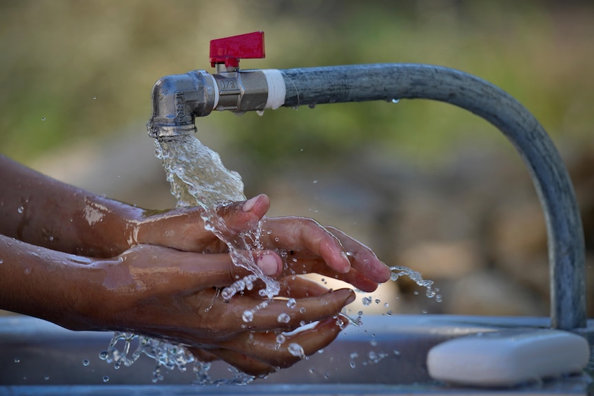 A pair of hands washing under a metal tap outside. 