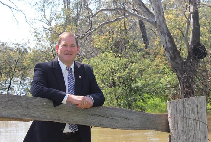 Nationals MP Tim McCurdy leans on an old fence near a river.