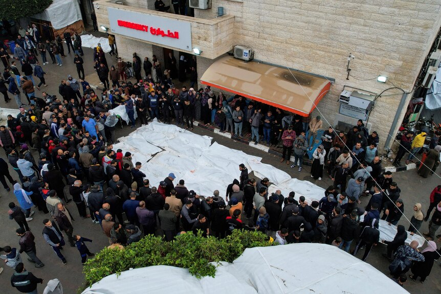 An aerial view of people gathered next to tarps covering bodies of dead Palestinians
