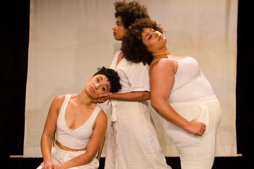 Production photograph of actors Ayeesha Ash, Emily Havea, Angela Sullen dress in all white posing on stage.
