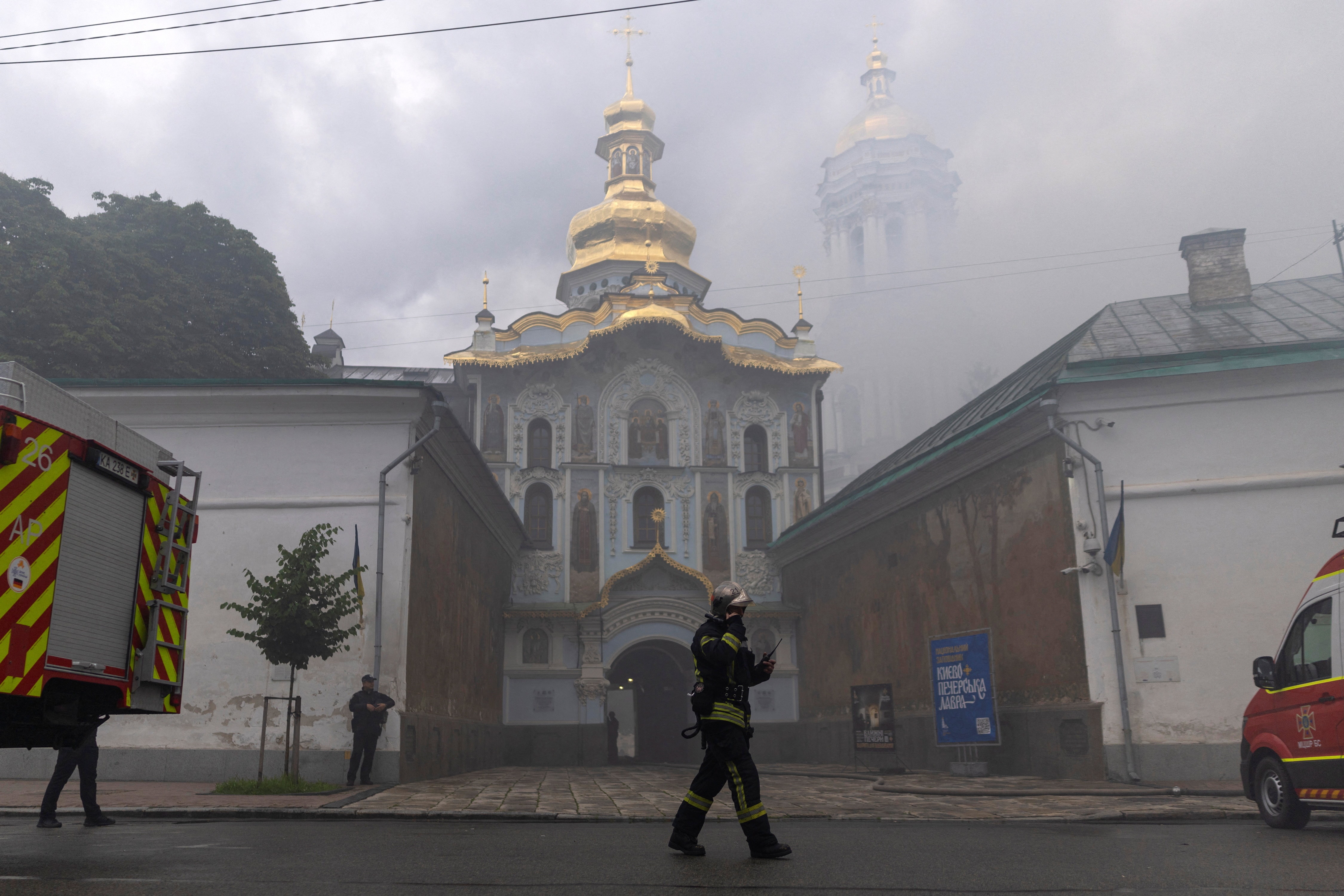 An emergency worker in front of a burning gold domed monastery.