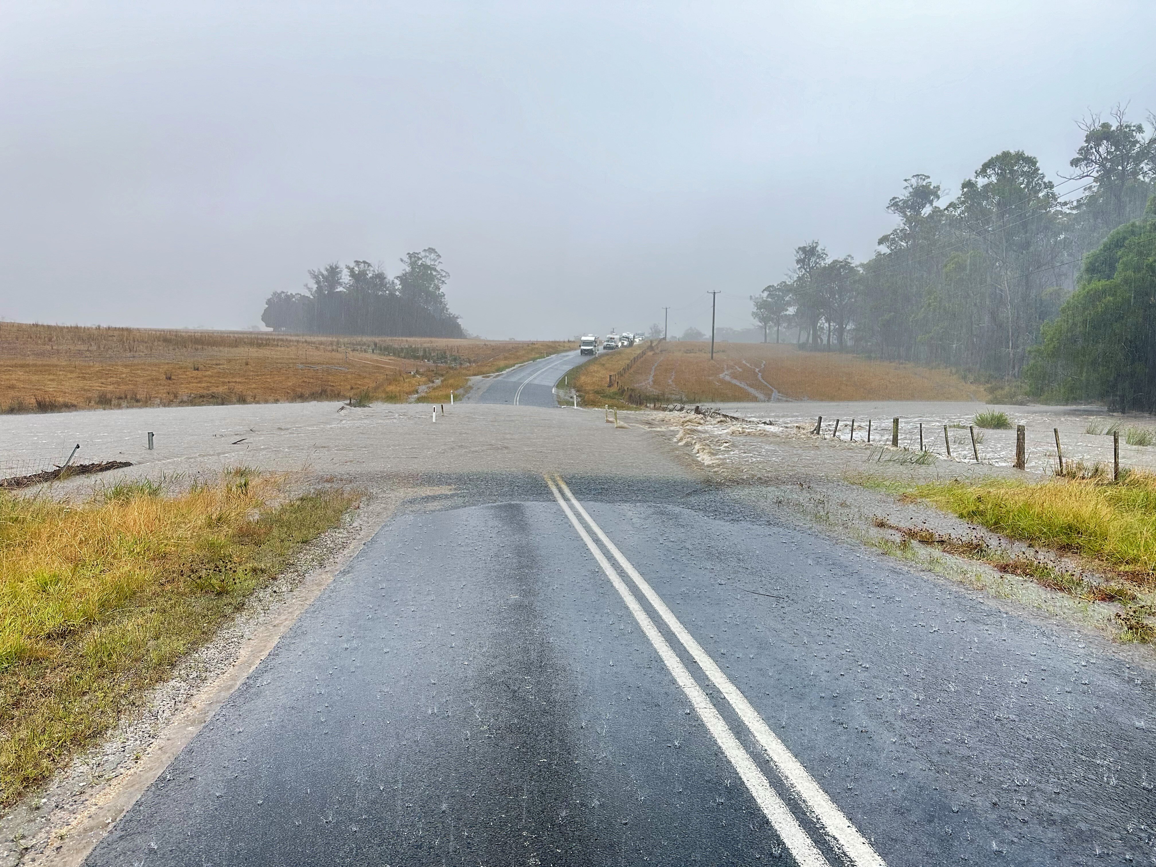 A road that is cut off by flooding, with cars waiting above the flood line.