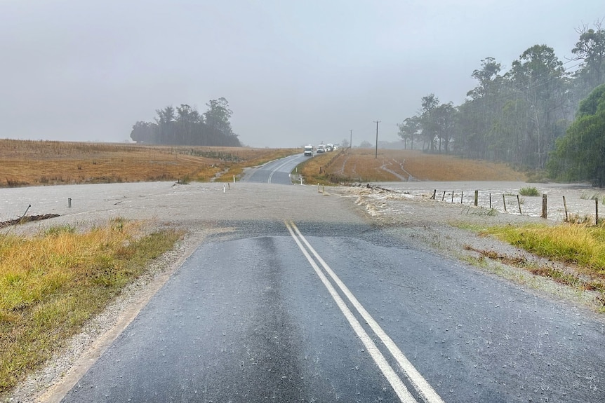 A road that is cut off by flooding, with cars waiting above the flood line.
