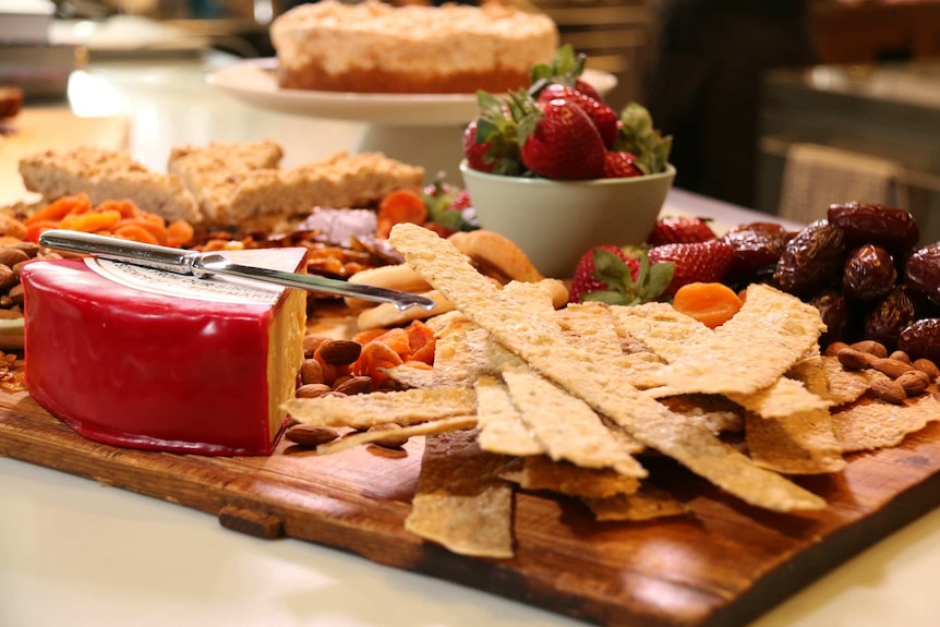 A cheese wheel and biscuits sit on a table full of food.