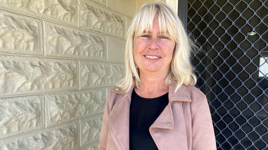 A woman with blonde hair stands on a front doorstep