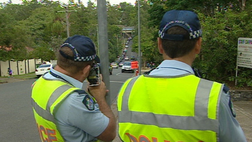 Generic TV still of back view of two Qld police officers pointing radar guns down Brisbane road.