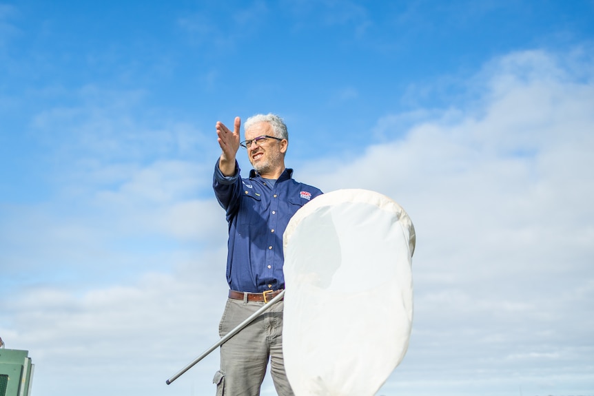 A man holding a large net points into the distance with the sky behind him.