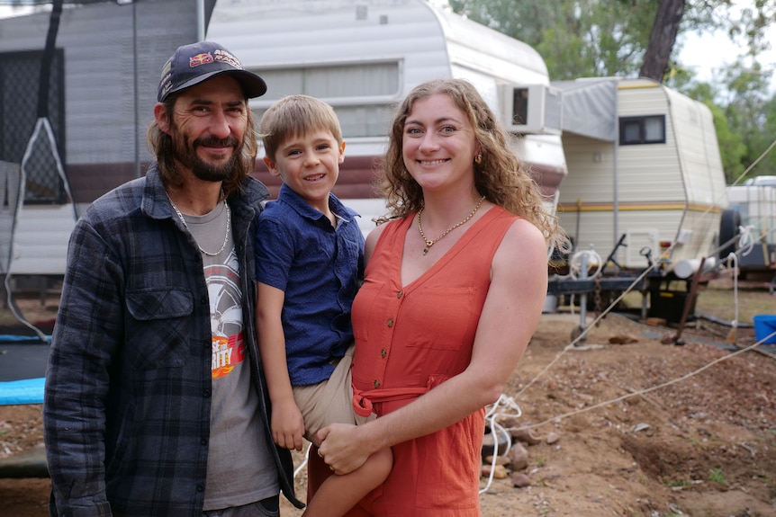 Matt and Amber holding their son, caravans behind.