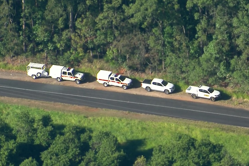 Emergency service vehicles line a road through a wooded area.