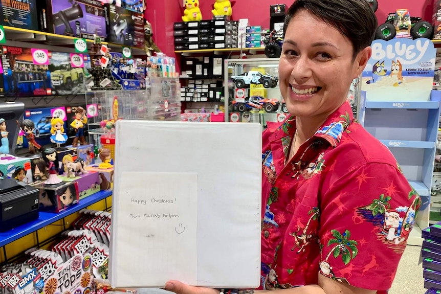 Staffer Rachael Thompson holds up the lay-by book at the toy store with a note from anonymous donors.