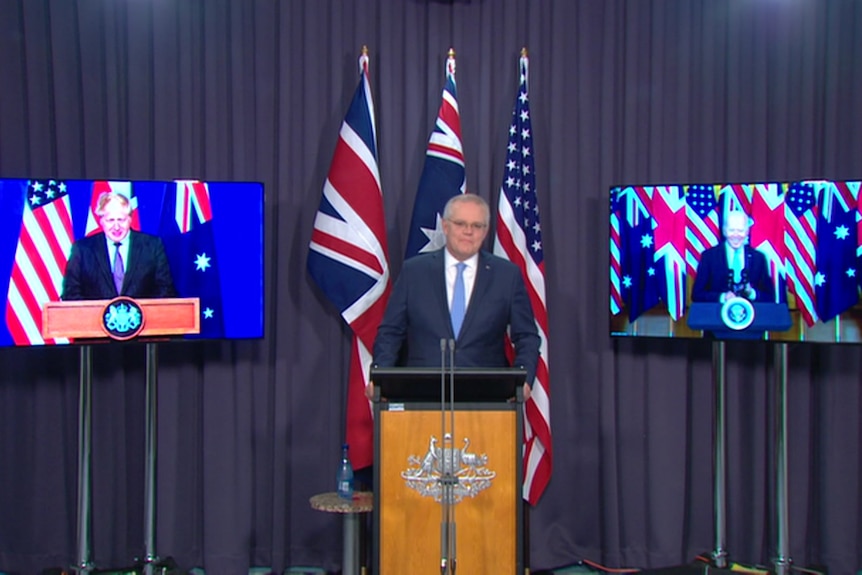 The Prime Minister stands between two TV screens displaying the UK and US leaders.