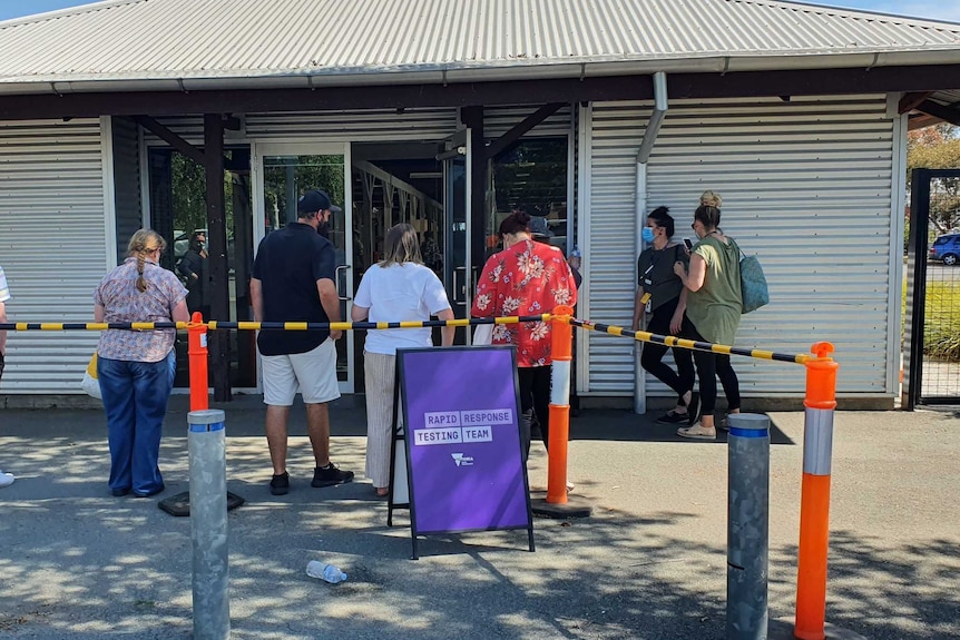 A line of people queuing outside a building with a purple sign that says "rapid response testing team".