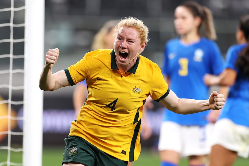 A Matildas players screams out and pumps her fists as she celebrates scoring a goal against Brazil.