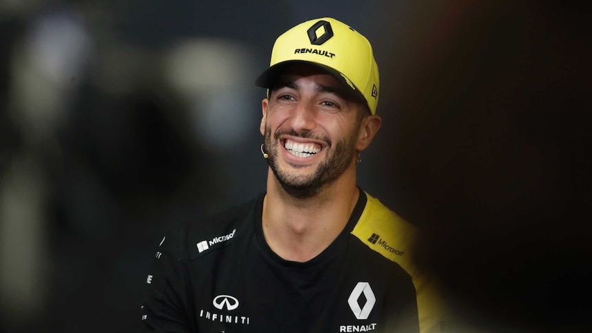 Daniel Ricciardo smiles with a yellow cap on his head and black t-shirt