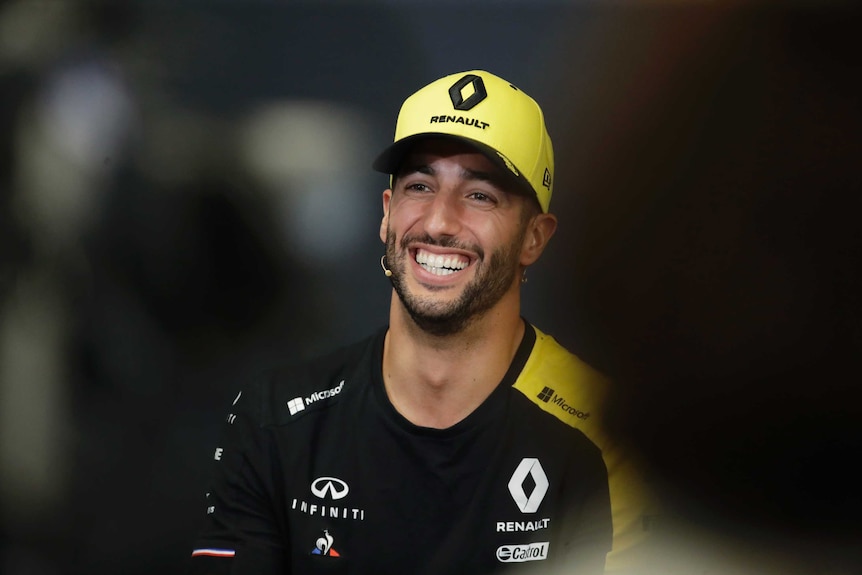 Daniel Ricciardo smiles with a yellow cap on his head and black t-shirt