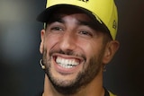 Daniel Ricciardo smiles with a yellow cap on his head and black t-shirt