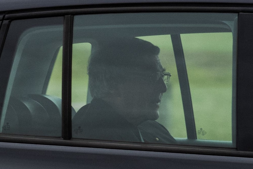George Pell sits in the back seat of a black car.