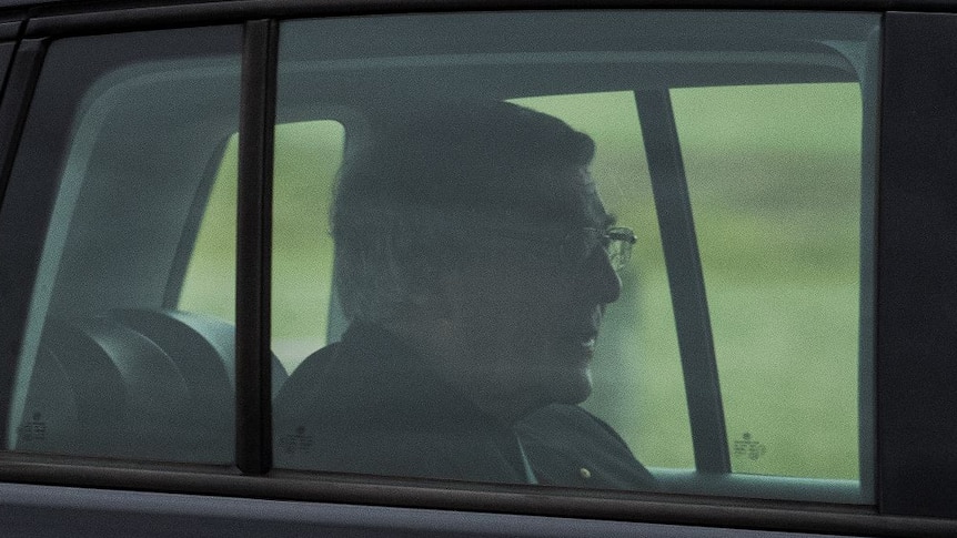 George Pell sits in the back seat of a black car.