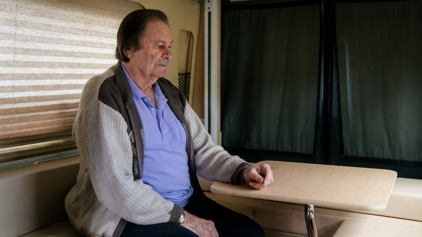 A man sits at a table inside a campervan looking downwards.