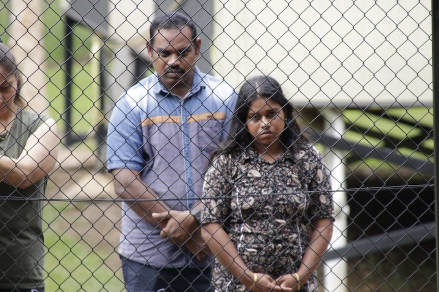 Detainees Parmika Sutharsan and Kirubakaran Rasanayagam stand behind a high wire fence.