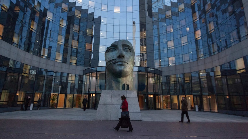 A curved glass building with a statue of a face in front