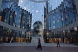 A curved glass building with a statue of a face in front