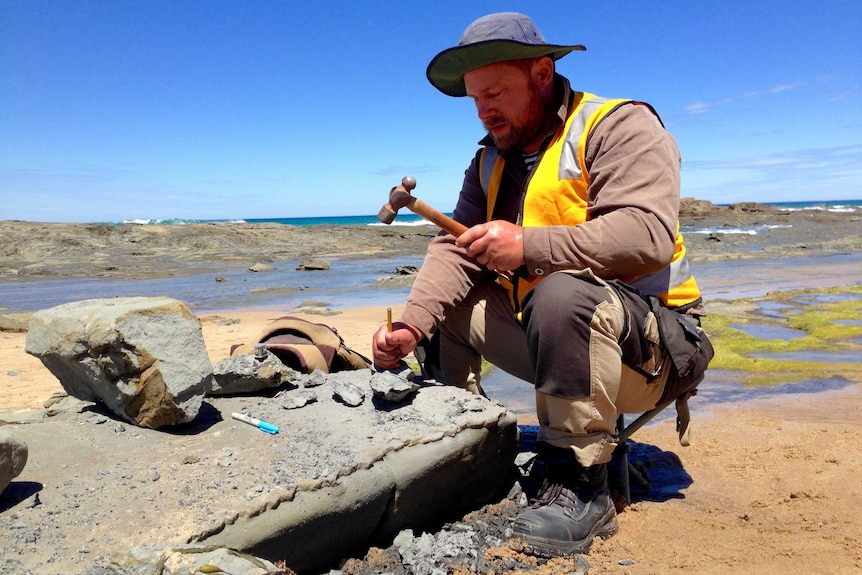 Dean Wright wields a hammer and chisel at a dig site.