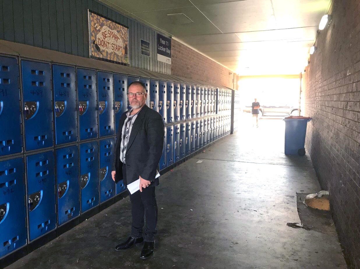 A man standing in a corridor beside school lockers.